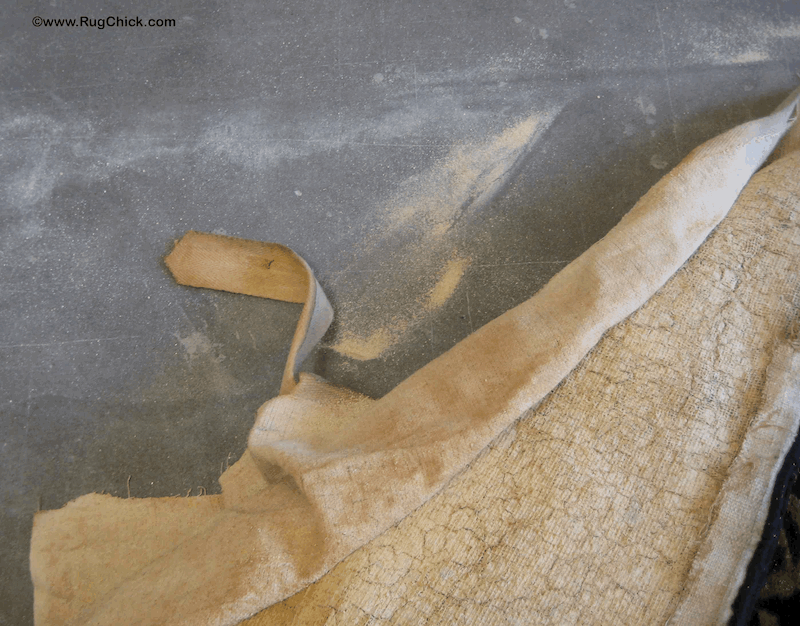 Back of a tufted rug with the material peeled back to expose the latex that is powdering and crumbling away after some age. 